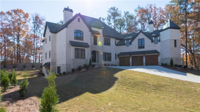 french provincial home with driveway, a chimney, an attached garage, a standing seam roof, and a front yard