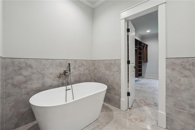 full bathroom featuring a soaking tub, ornamental molding, marble finish floor, and tile walls