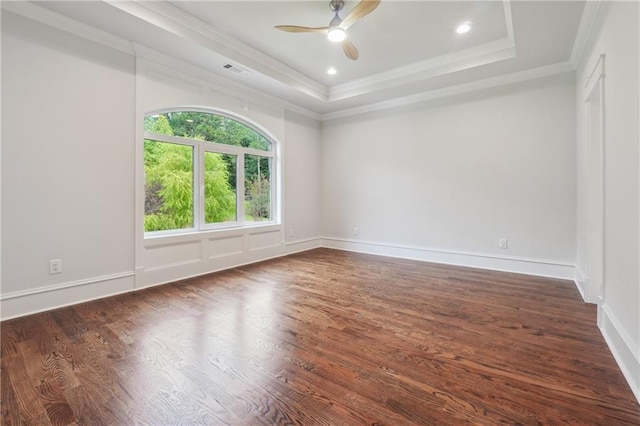 empty room with a ceiling fan, a tray ceiling, dark wood finished floors, and crown molding