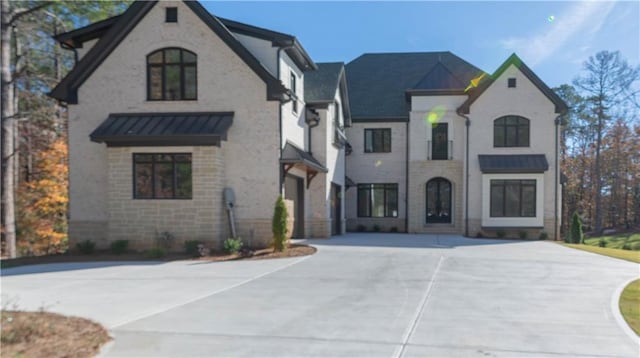 french provincial home featuring a standing seam roof, brick siding, metal roof, and concrete driveway