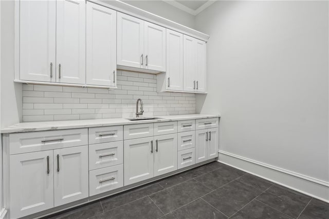 kitchen featuring dark tile patterned flooring, a sink, white cabinetry, baseboards, and backsplash