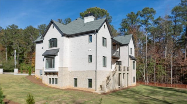 view of side of home with a balcony, a chimney, and a yard