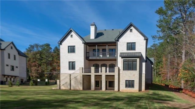 back of property featuring a balcony, a standing seam roof, a chimney, and a lawn