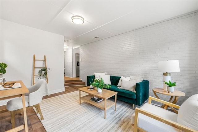 living room featuring baseboards, brick wall, visible vents, and light wood-style flooring