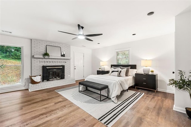 bedroom featuring ceiling fan, a fireplace, baseboards, wood finished floors, and visible vents