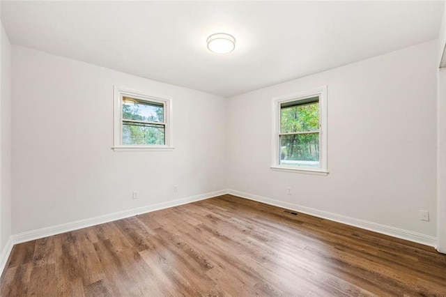 empty room featuring baseboards, wood finished floors, a healthy amount of sunlight, and visible vents