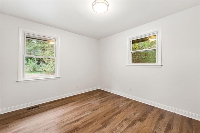 spare room featuring a healthy amount of sunlight, baseboards, wood finished floors, and visible vents