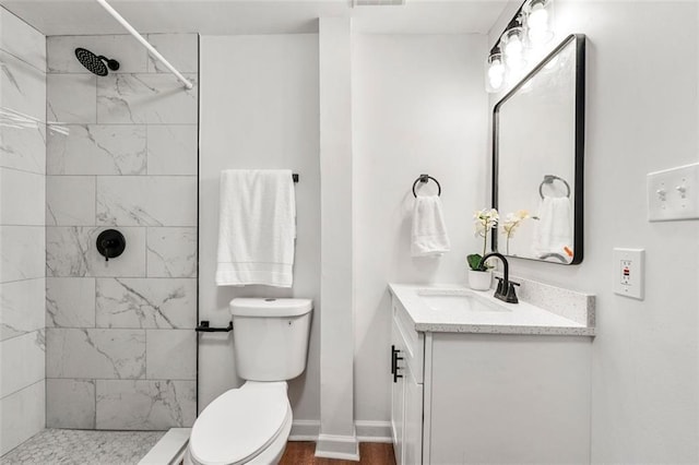 full bath featuring a tile shower, wood finished floors, vanity, baseboards, and toilet