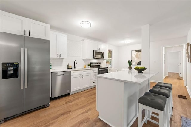 kitchen with white cabinets, appliances with stainless steel finishes, light countertops, a breakfast bar area, and light wood-type flooring