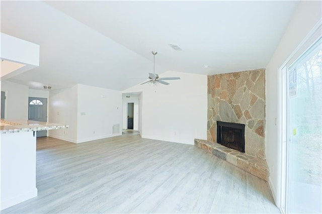 unfurnished living room featuring a stone fireplace, light hardwood / wood-style flooring, ceiling fan, and vaulted ceiling