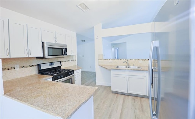 kitchen with sink, white cabinetry, kitchen peninsula, stainless steel appliances, and light hardwood / wood-style floors