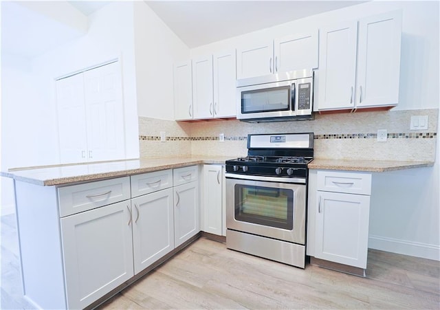 kitchen with light wood-type flooring, kitchen peninsula, white cabinets, and appliances with stainless steel finishes