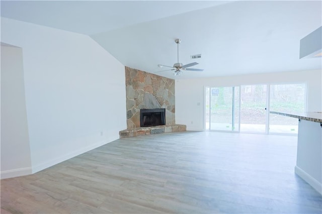 unfurnished living room with lofted ceiling, a stone fireplace, light hardwood / wood-style flooring, and ceiling fan