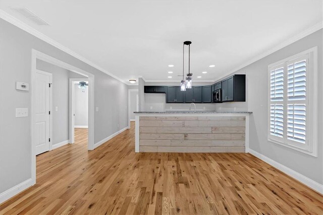 kitchen featuring crown molding, stainless steel microwave, light wood-style flooring, and light stone countertops