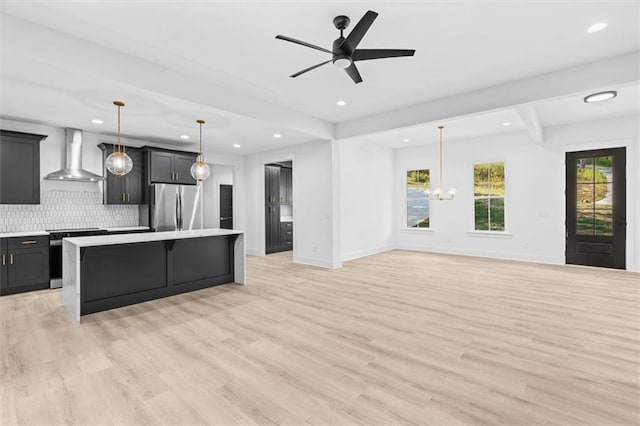 kitchen featuring a kitchen island, wall chimney range hood, hanging light fixtures, light wood-type flooring, and appliances with stainless steel finishes