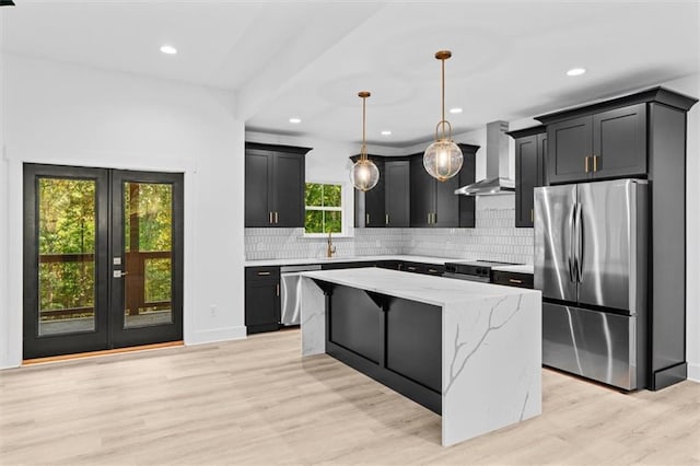 kitchen with a center island, hanging light fixtures, stainless steel appliances, wall chimney exhaust hood, and light hardwood / wood-style flooring