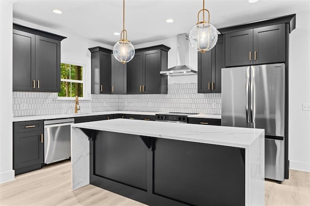 kitchen with wall chimney range hood, stainless steel appliances, hanging light fixtures, and light wood-type flooring