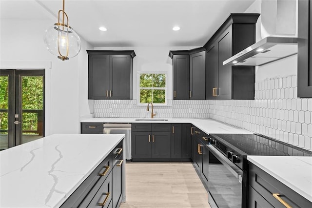 kitchen with wall chimney range hood, appliances with stainless steel finishes, light wood-type flooring, pendant lighting, and sink