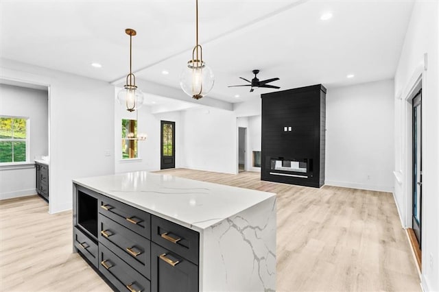 kitchen with a kitchen island, pendant lighting, light stone counters, light hardwood / wood-style floors, and ceiling fan