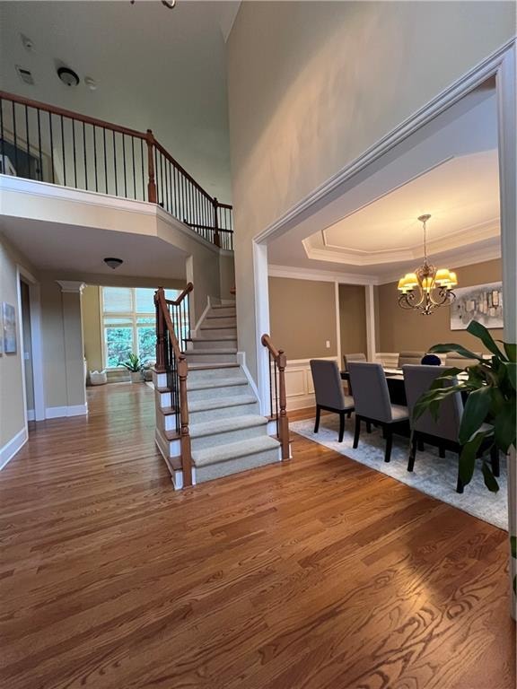 staircase featuring crown molding, a chandelier, a high ceiling, and hardwood / wood-style flooring