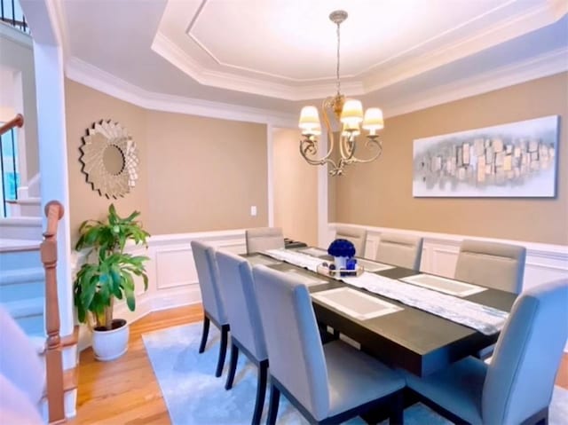 dining area featuring light hardwood / wood-style flooring, an inviting chandelier, a tray ceiling, and crown molding