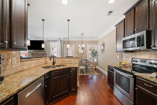 kitchen with sink, dark brown cabinets, light stone counters, appliances with stainless steel finishes, and pendant lighting