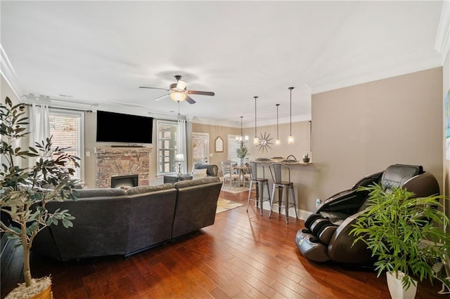 living room featuring ceiling fan, crown molding, dark hardwood / wood-style floors, and a stone fireplace