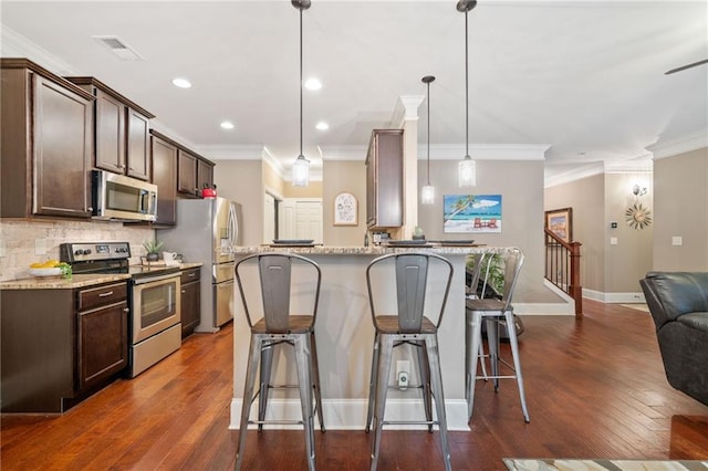 kitchen with decorative light fixtures, light stone counters, appliances with stainless steel finishes, a breakfast bar area, and decorative backsplash