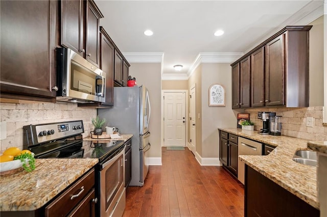 kitchen featuring appliances with stainless steel finishes, light stone counters, crown molding, dark hardwood / wood-style flooring, and dark brown cabinets