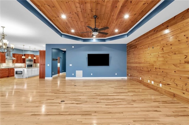 1580 Loving Rd, Morganton, GA 30560 - unfurnished living room with visible vents, wood walls, ceiling fan with notable chandelier, a tray ceiling, and light wood-style flooring