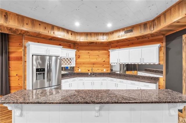1580 Loving Rd, Morganton, GA 30560 - kitchen with a kitchen breakfast bar, stainless steel fridge with ice dispenser, dark stone countertops, wooden walls, and white cabinetry