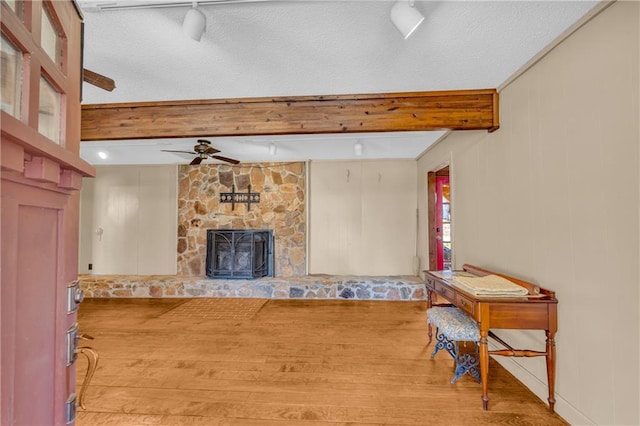 living room featuring light hardwood / wood-style floors, ceiling fan, a fireplace, a textured ceiling, and beamed ceiling