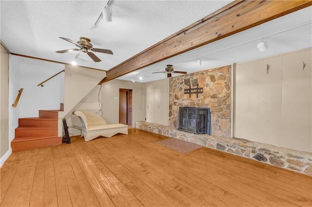 unfurnished living room featuring ceiling fan, a fireplace, wood-type flooring, a textured ceiling, and rail lighting