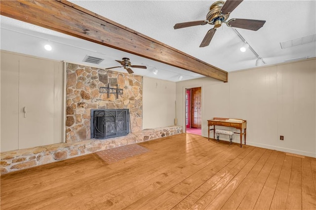 unfurnished living room with hardwood / wood-style floors, beam ceiling, a stone fireplace, track lighting, and a textured ceiling