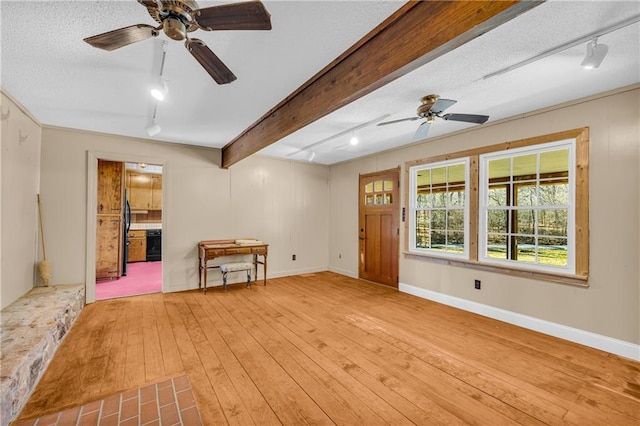 unfurnished living room with rail lighting, ceiling fan, light wood-type flooring, a textured ceiling, and beamed ceiling