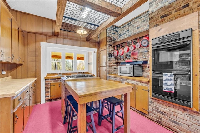 kitchen with black double oven, beamed ceiling, wood walls, light colored carpet, and butcher block countertops