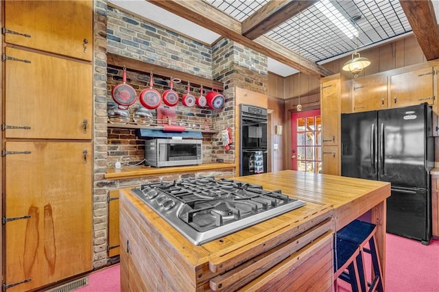 kitchen featuring brick wall, carpet flooring, beam ceiling, and black appliances