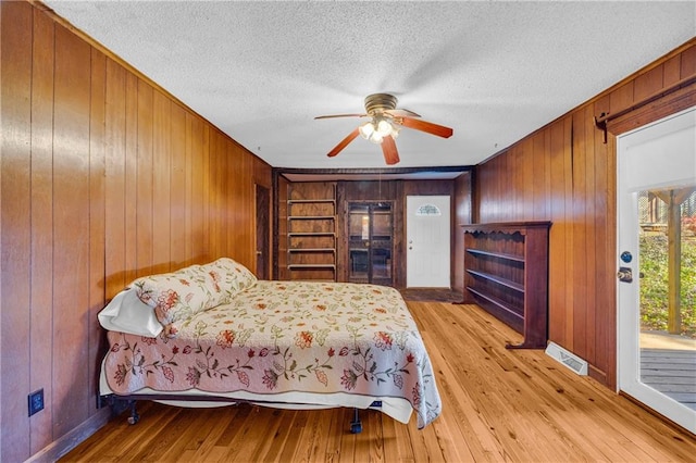 bedroom with ceiling fan, a textured ceiling, light wood-type flooring, and wooden walls