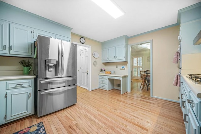 kitchen with light wood finished floors, appliances with stainless steel finishes, ornamental molding, and light countertops