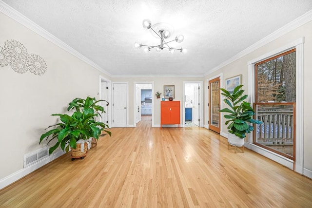 unfurnished room with light wood-type flooring, visible vents, a textured ceiling, and ornamental molding