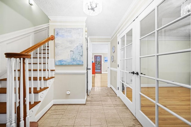 hallway with a wainscoted wall, french doors, stairway, crown molding, and a decorative wall