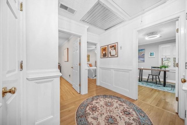 hallway with visible vents, light wood-style flooring, attic access, and ornamental molding