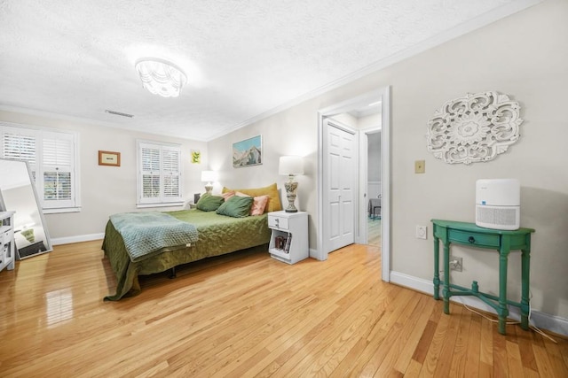 bedroom featuring light wood-style flooring, ornamental molding, baseboards, and a textured ceiling