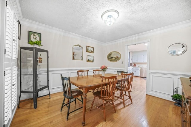 dining space featuring a wainscoted wall, a textured ceiling, light wood-type flooring, and ornamental molding