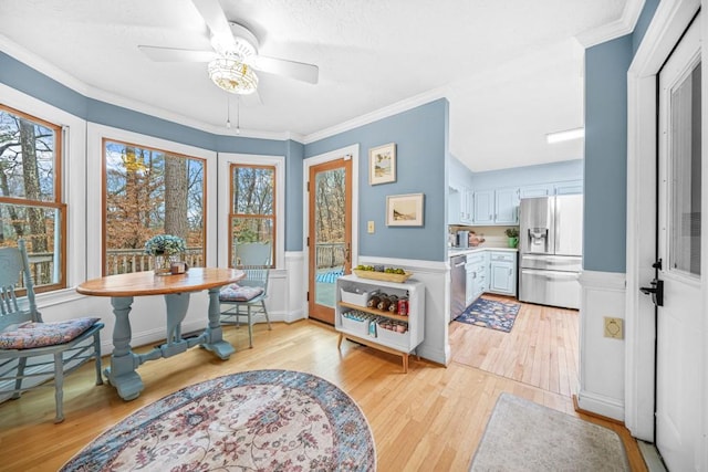 dining room with a wainscoted wall, crown molding, a ceiling fan, and light wood-type flooring