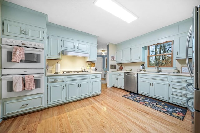 kitchen with light wood-style flooring, a sink, under cabinet range hood, appliances with stainless steel finishes, and light countertops