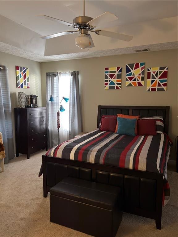 bedroom with a tray ceiling, visible vents, carpet, and a ceiling fan