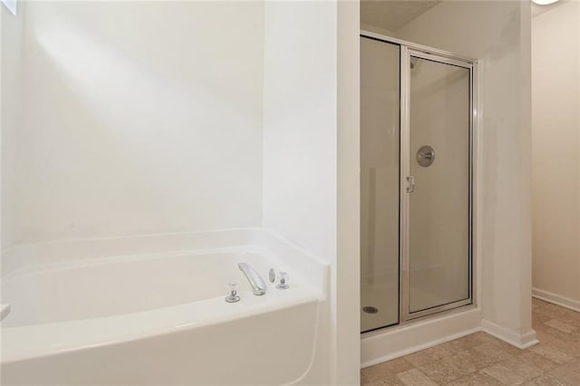 bathroom with a shower stall, a garden tub, and baseboards