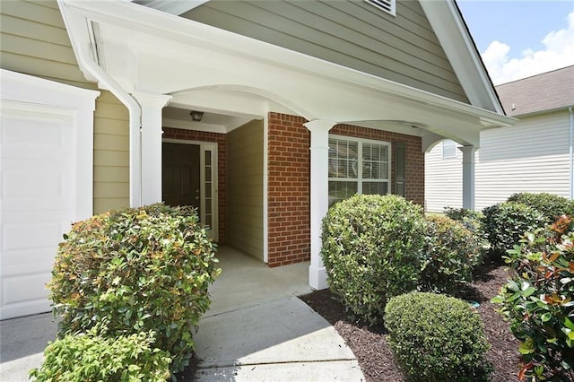 view of exterior entry featuring a garage, brick siding, and covered porch