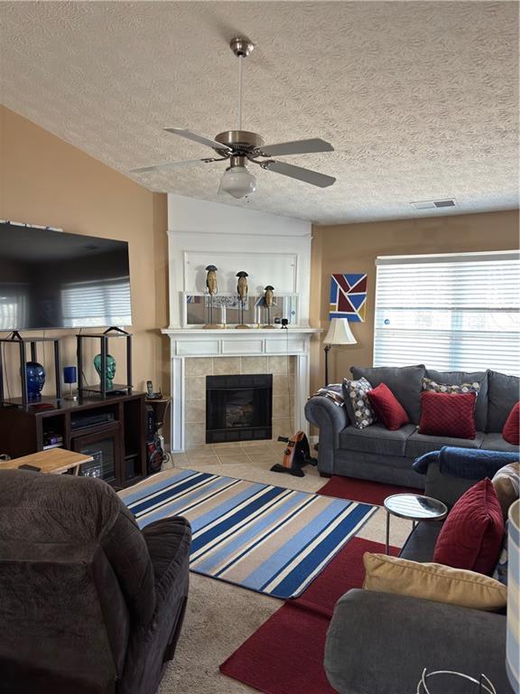 carpeted living room with visible vents, a ceiling fan, a tiled fireplace, a textured ceiling, and lofted ceiling